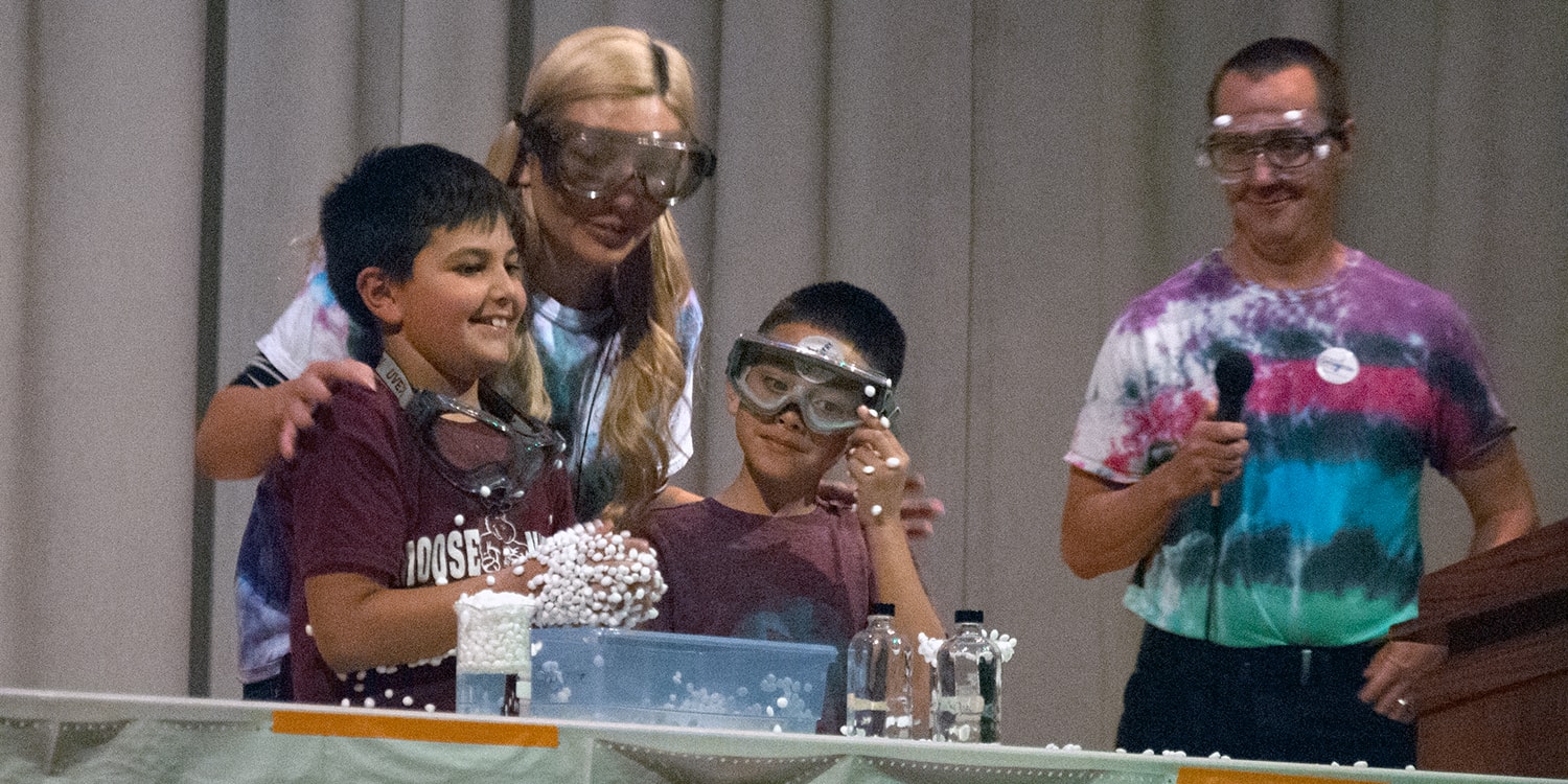 college students help young students with chemistry experiment