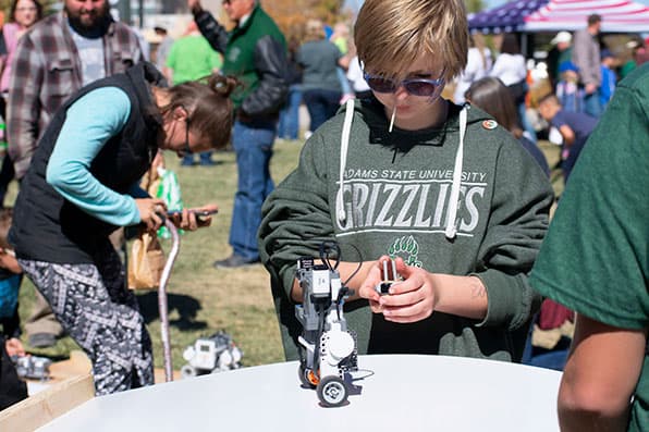 Young person in Adams State hoodie works with small robot