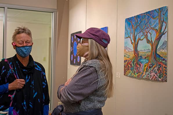 Two masked women talk in front of paintings