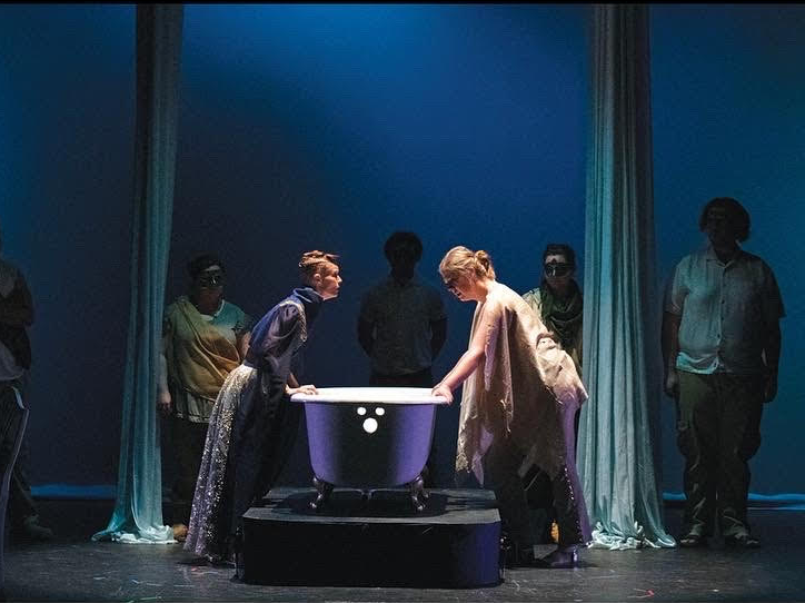 Two people stand over a bathtub and talk as others stand in the darkened background behind them on the Adams State theatre during a production of "Clyt; or, The Bathtub Play" by Elisabeth Giffin Speckman.