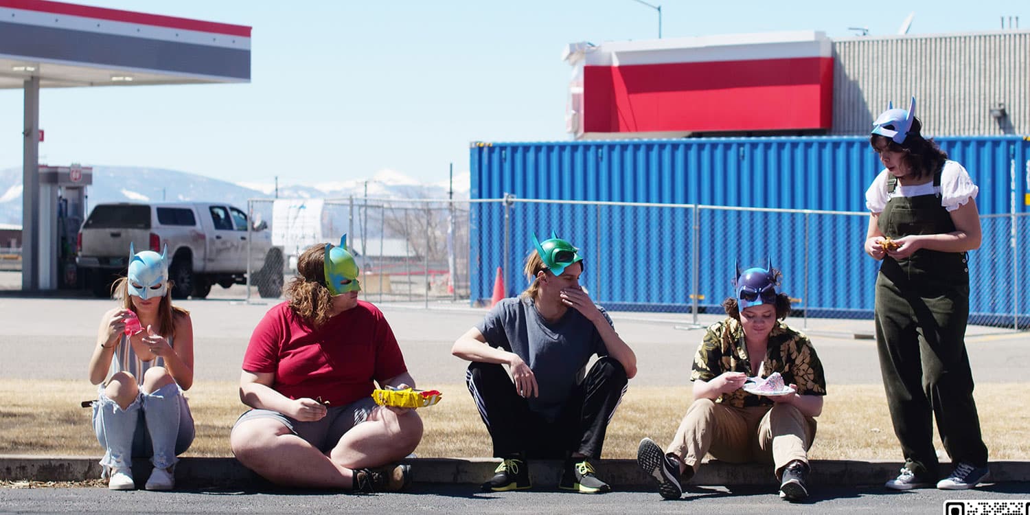 Adams State Theatre students wearing masks sitting on curb