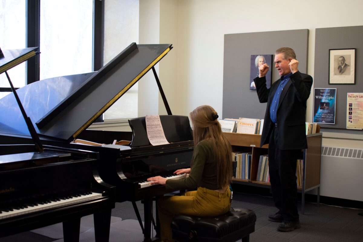 A music professor gestures enthusiastically as a student plays piano.