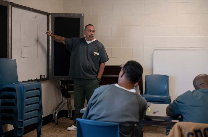 The first Incarcerated Instructor ponts to a whiteboard while teaching students at Colorado Territorial Correctional Facility in Colorado.