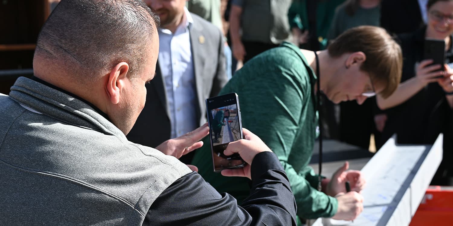 Adams State University Computing Services Building Beam Topping Ceremony, Dr. Savala DeVoge signing beam, Dr. Florencio Urias Aranda taking a video