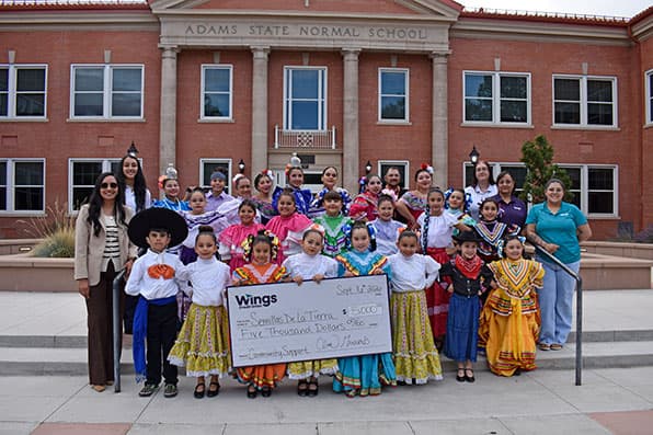Adams State University Semillas de la Tierra dancers and Wings Credit Union representatives pose in front of Richardson Hall