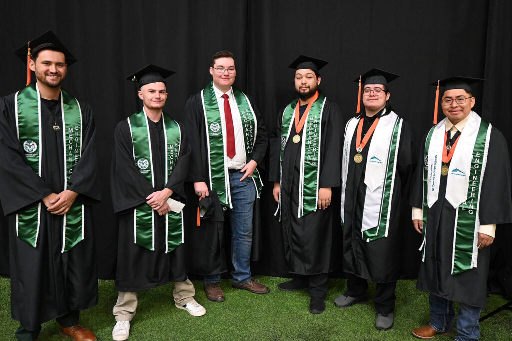 Adams State University & Colorado State University first mechanical engineering graduates in caps and gowns before black background